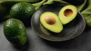 Aguacates abiertos encima de un plato y aguacates enteros.